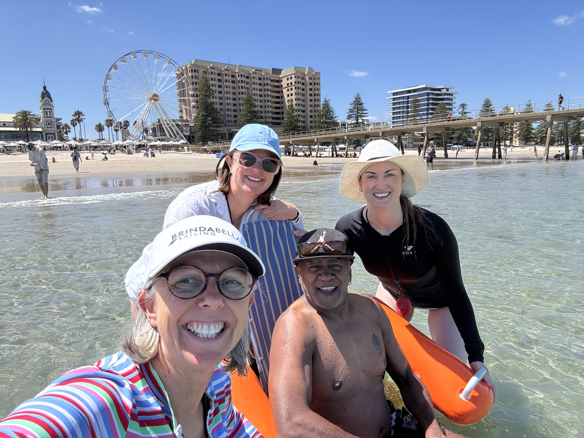 Three LSA staff members with a LSS participant in a floating wheelchair at Glenelg Beach.